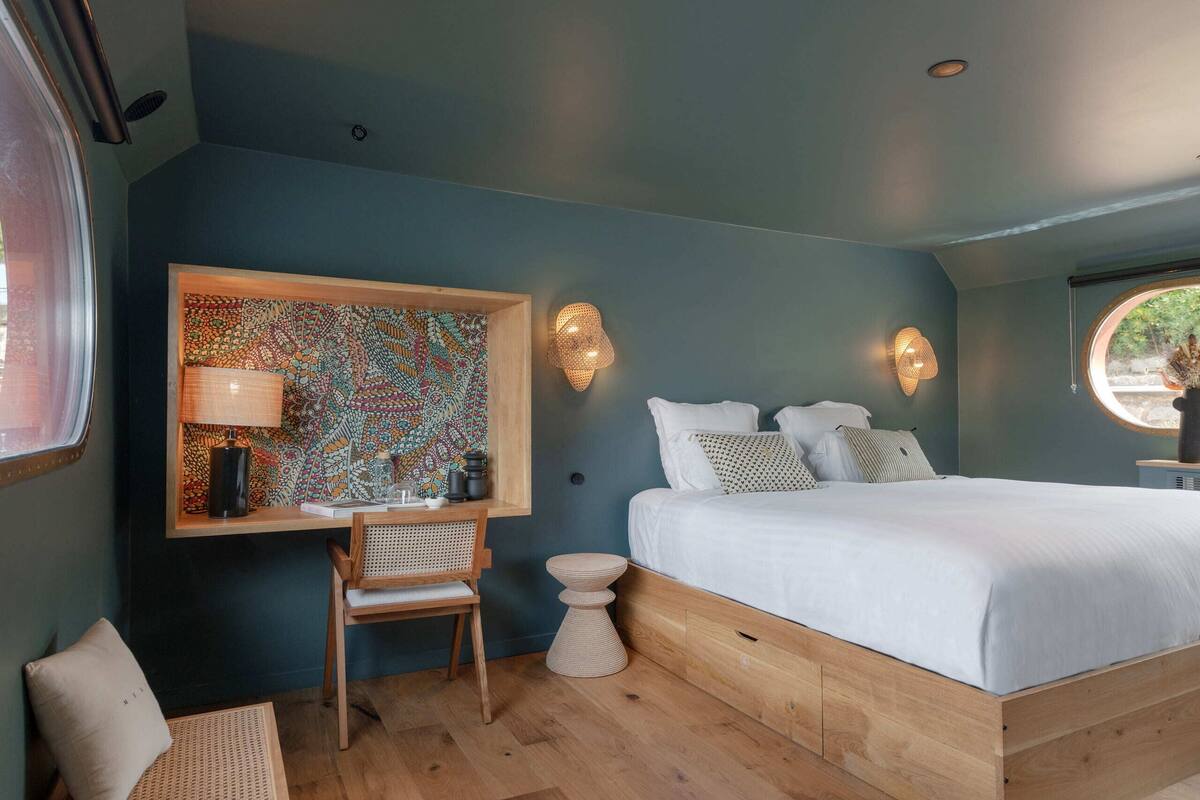 A bedroom with a bed, a desk, a chair, and a wall-mounted lamp.