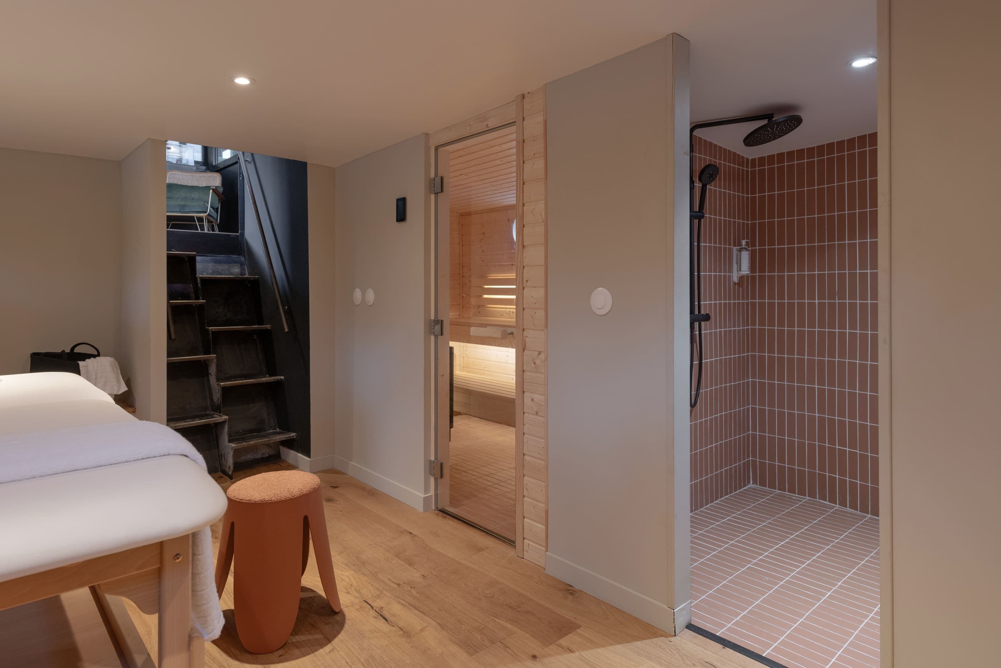 Une chambre à coucher comprenant un lit, un tabouret en bois, une armoire et un espace douche avec des murs carrelés.
