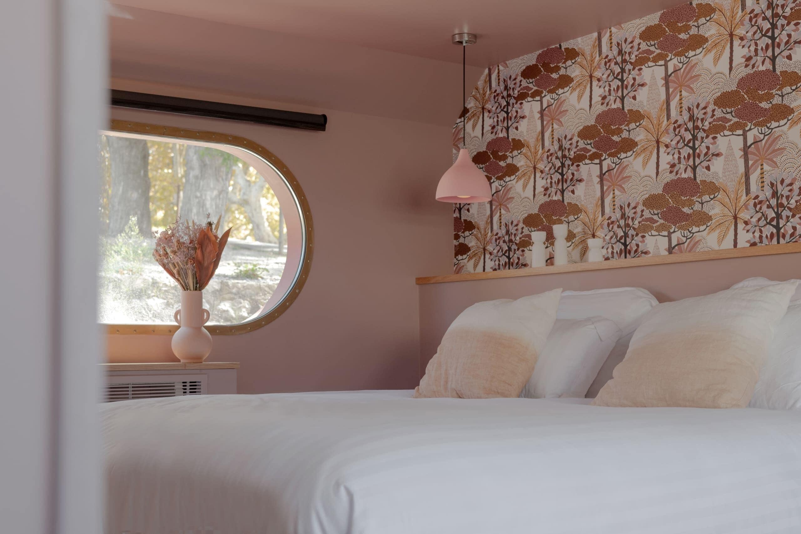 Un dormitorio con cama, un ventanal redondo, una lámpara de pared y un papel tapiz floral.