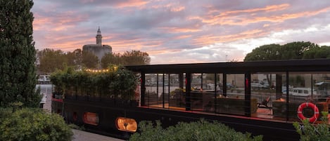 A boat with a glass facade, surrounded by greenery, and a distant tower.