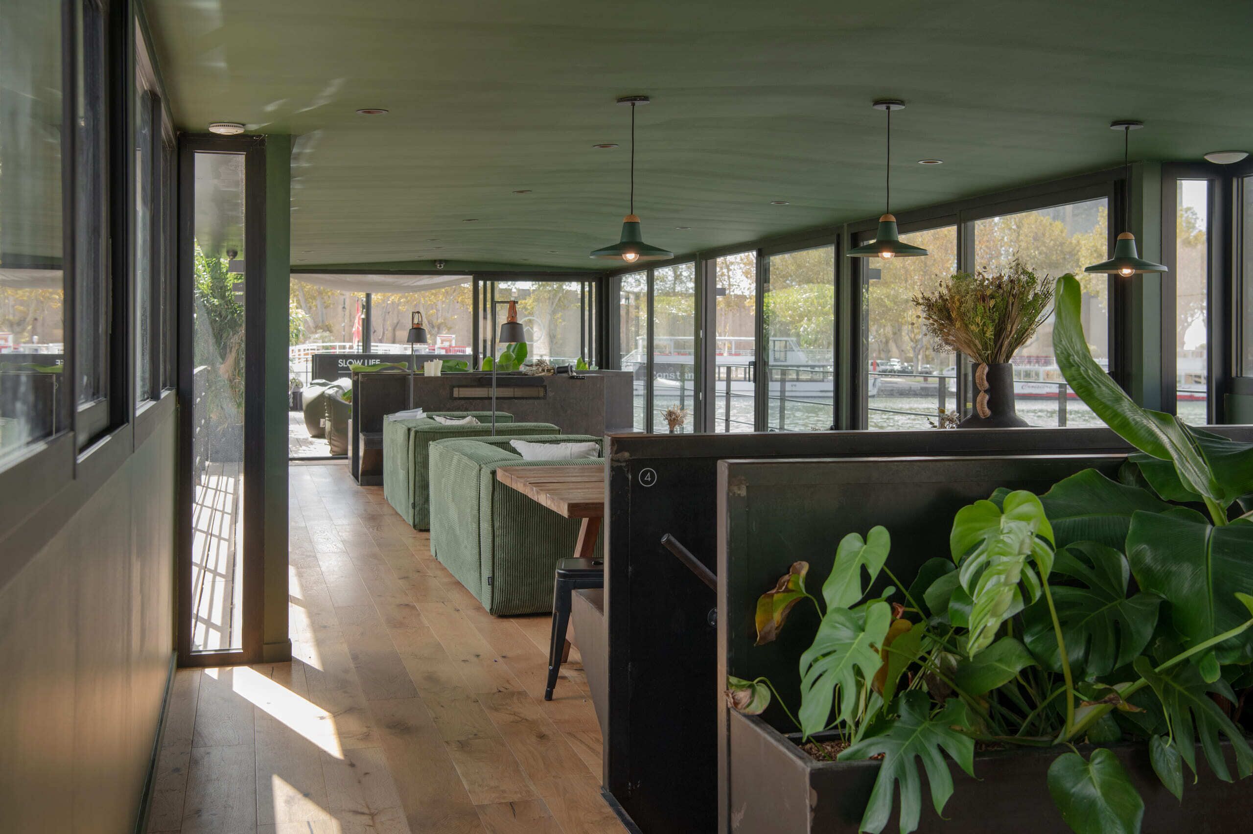 A modern interior with large windows, wooden flooring, and green upholstered seating.
