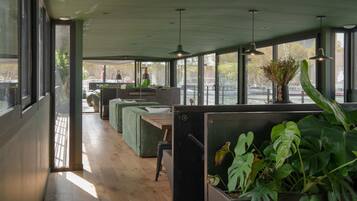 A modern interior with large windows, wooden flooring, and green upholstered seating.