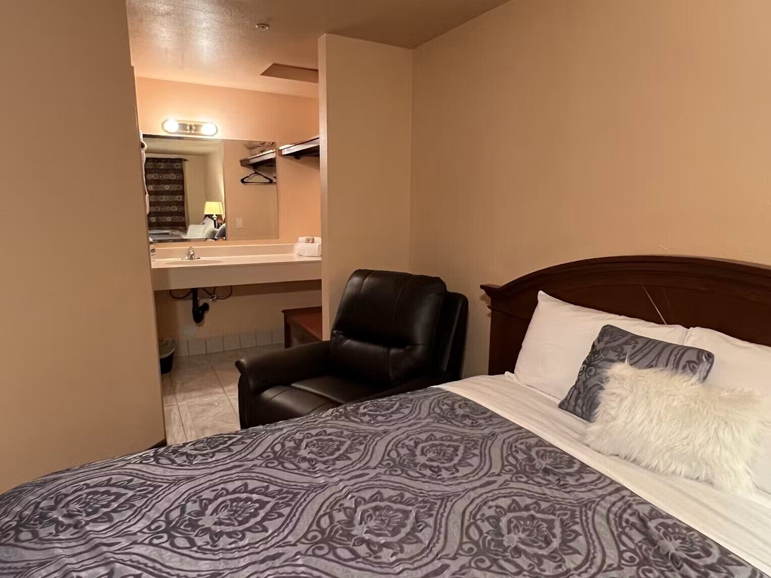 A hotel room with a bed, a chair, a vanity with a mirror, and a sink.
