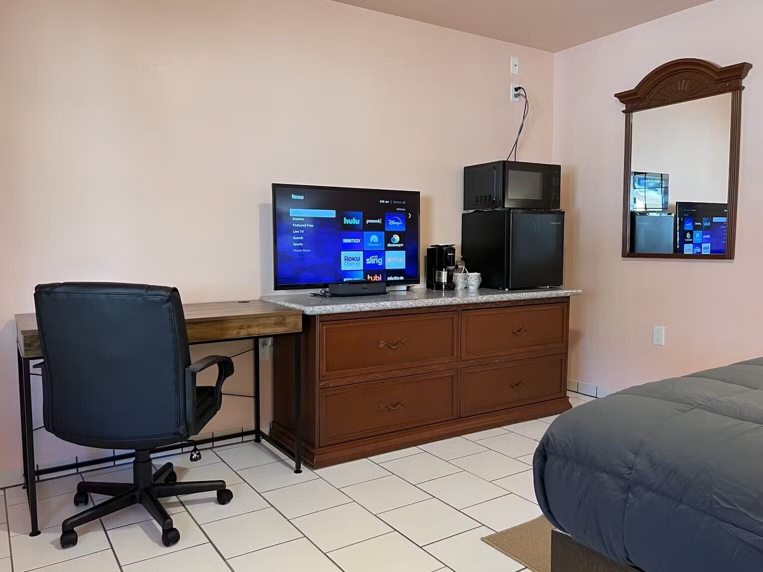A hotel room with a desk, computer, chair, minibar, and a bed.