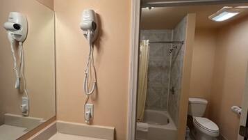 Ein Badezimmer mit Föhn, Badewanne, Toilette und Duschbereich.