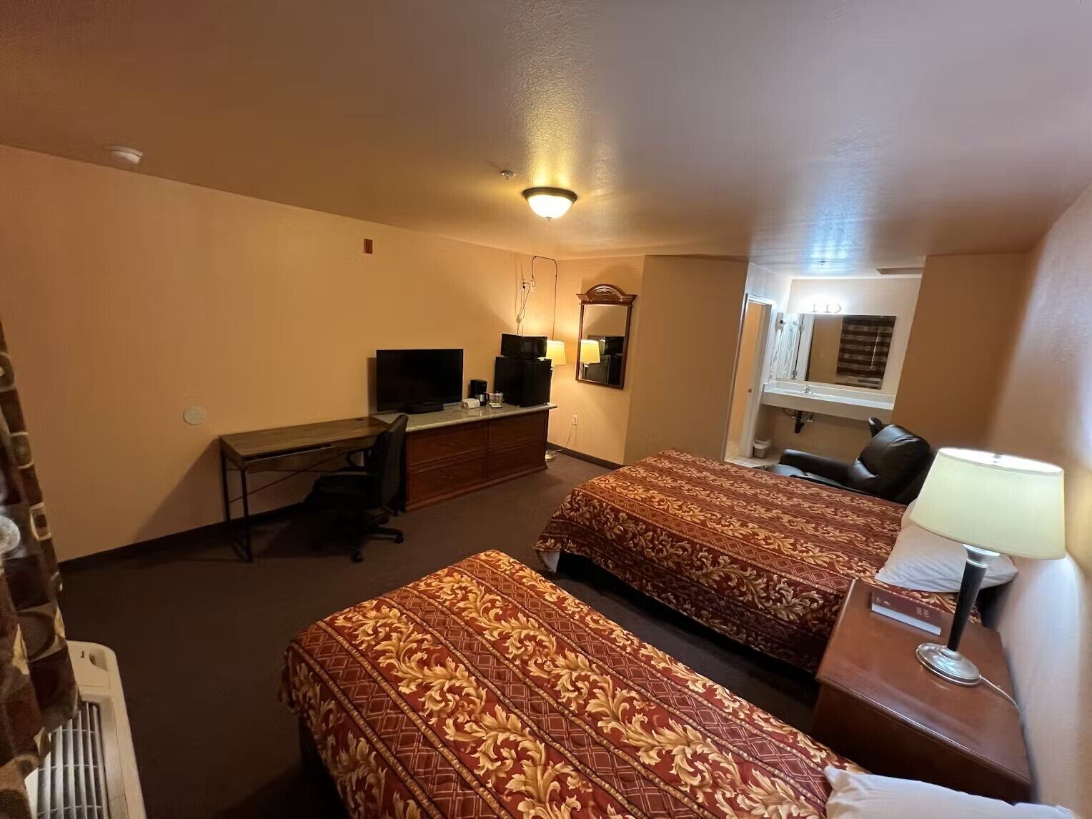 A hotel room with two beds, a desk with a computer, a TV, and a mirror.