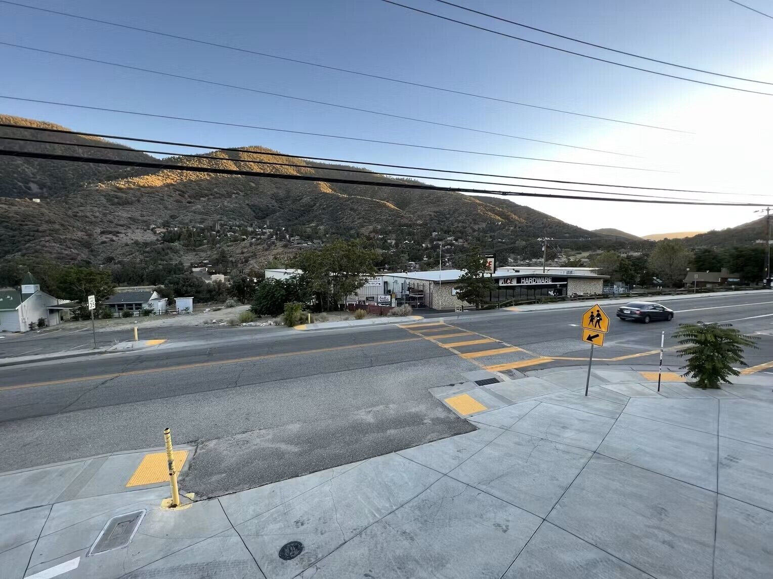 A road with a pedestrian crossing, a hardware store, and a mountain in the background.