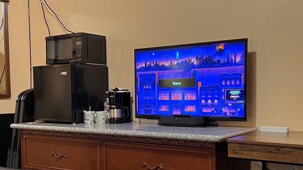 A hotel room with a television displaying a cityscape, a coffee maker, and a refrigerator on a wooden cabinet. - Frazier View Motel (Frazier Park)