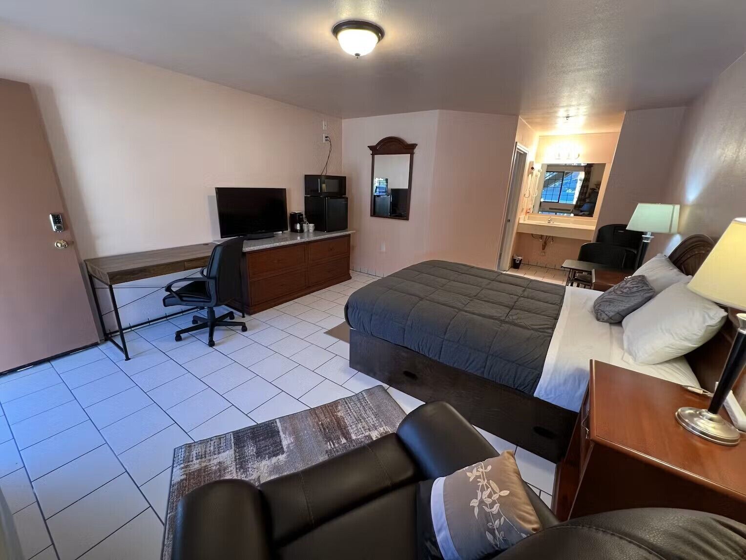A hotel room with a bed, desk, chair, TV, and a bathroom.