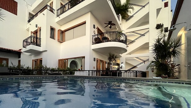 Un hotel de varios niveles con piscina central, balcones y plantas de interior.