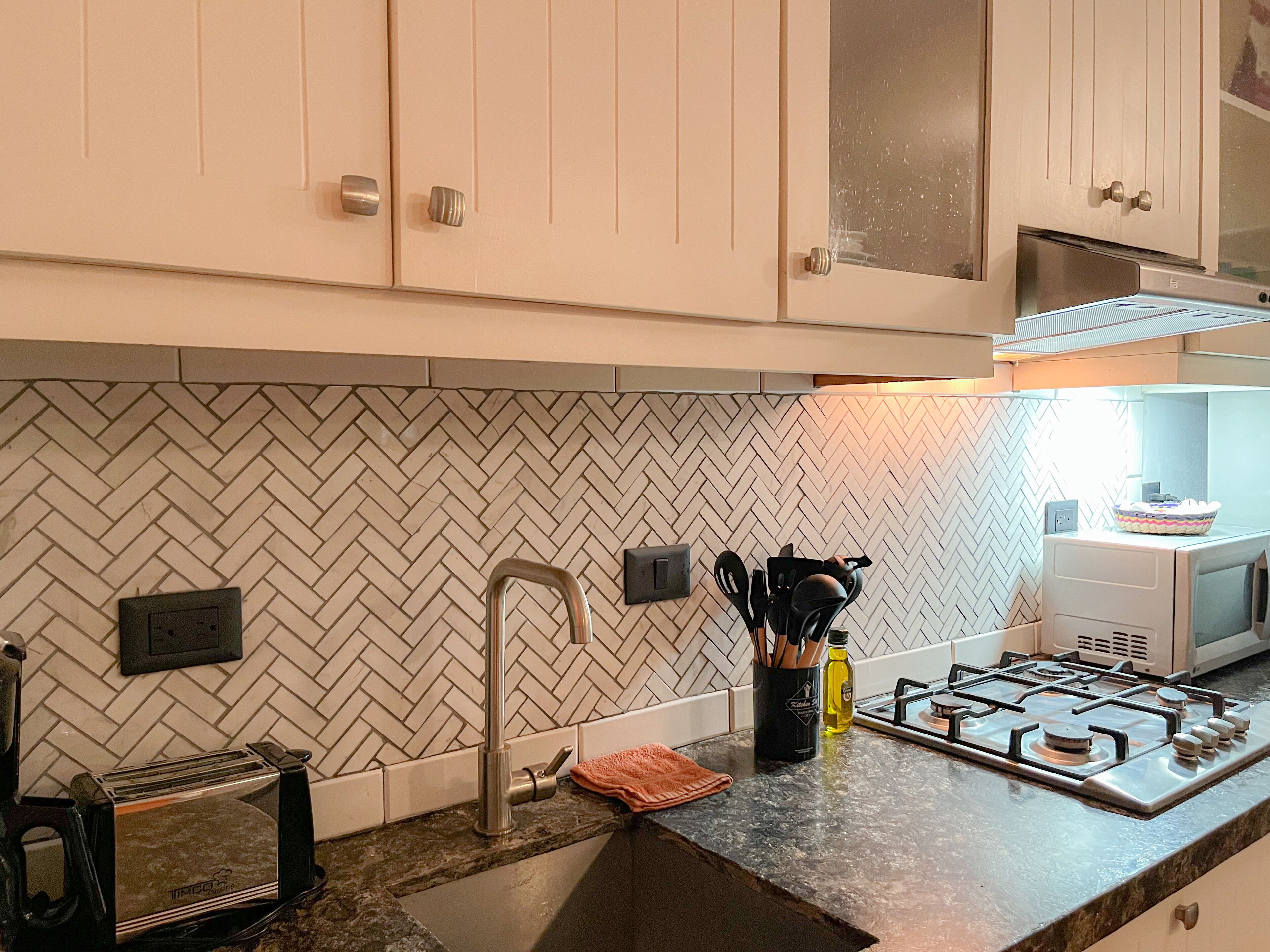 A kitchen with white cabinets, a herringbone backsplash, a gas stove, a toaster, and a sink.