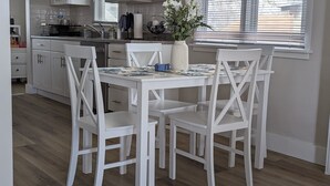 A dining area with a white table and chairs, a vase with flowers, and a kitchen in the background. - Quaint Murray Home- 2 bed/1 bath  20 min to ski/hike or downtown. 5 min to IMC. (Murray)