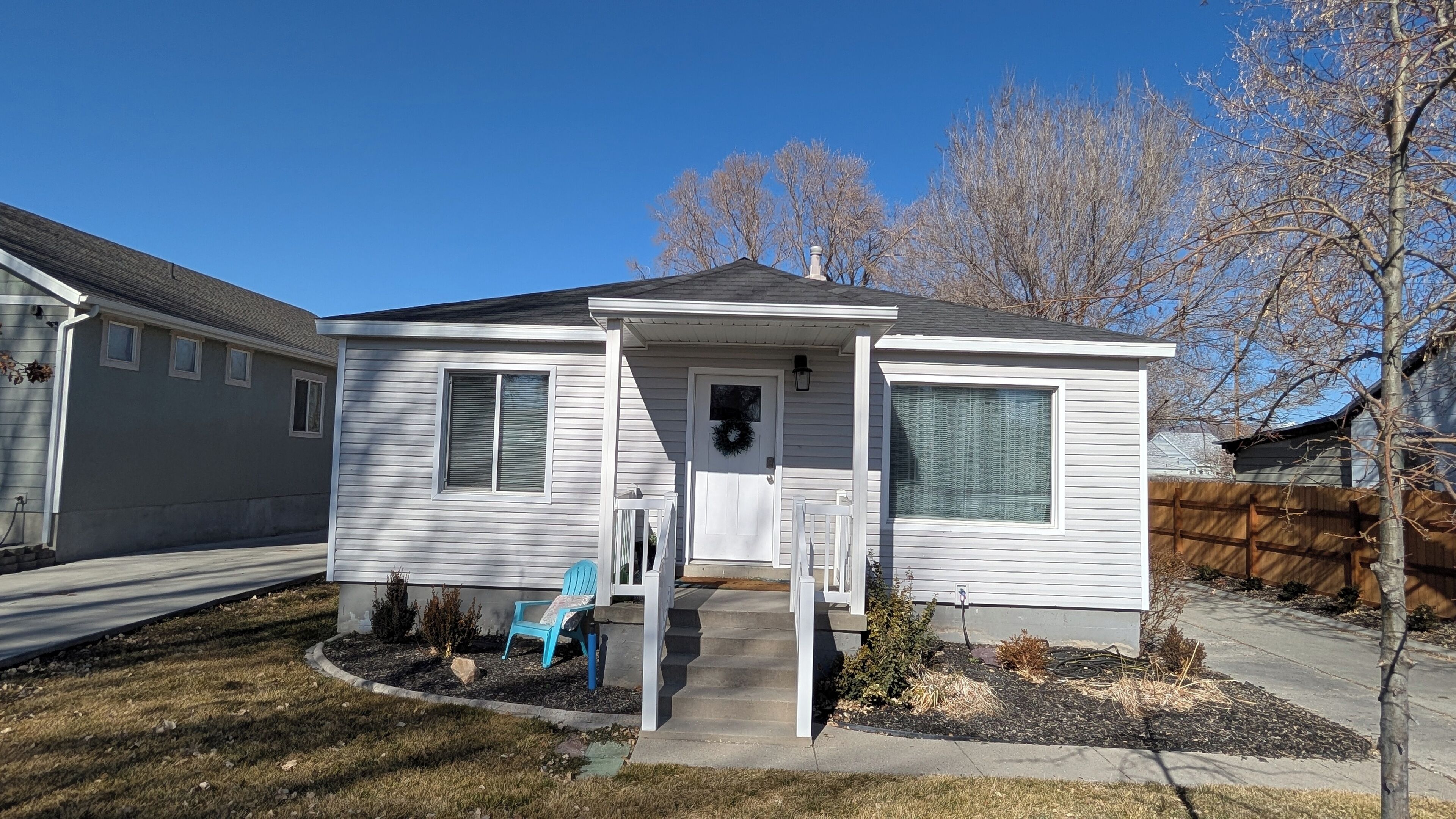 A single-story mobile home with a front porch, a small garden, and a blue chair.