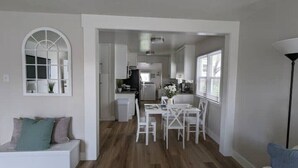 A modern kitchen with white cabinetry, a dining area with a white table and chairs, and a large window providing natural light. - Quaint Murray Home- 2 bed/1 bath  20 min to ski/hike or downtown. 5 min to IMC. (Murray)