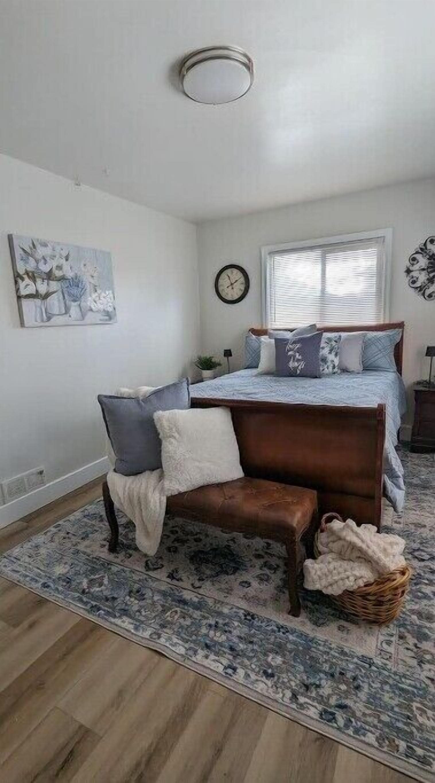A bedroom with a wooden bed, a bench, a rug, and a painting on the wall.