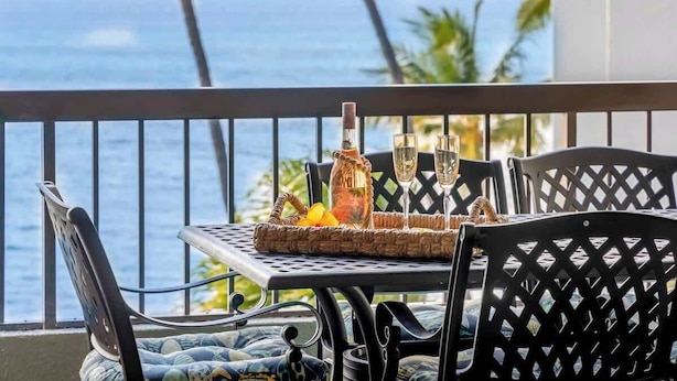 A balcony with a table set for two, featuring a bottle and glasses, overlooking the ocean.