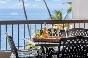 A balcony with a table set for two, featuring a bottle and glasses, overlooking the ocean. - Spacious top floor beachfront view 2 bedroom condo, private beach, walkable area (Napili-Honokowai)