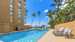 A swimming pool with lounge chairs and umbrellas, surrounded by palm trees and a building. - 1 bedroom Beachfront Condo, AC, Lanai Oceanview, 6 mile sandy beach (Kihei)