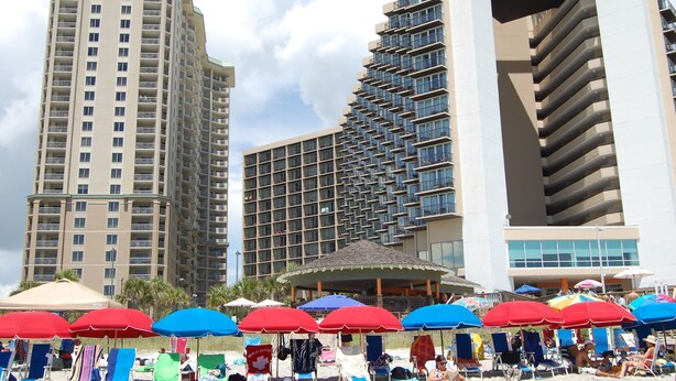 Un hotel con varios edificios altos, una zona de playa con sombrillas y sillas de playa.