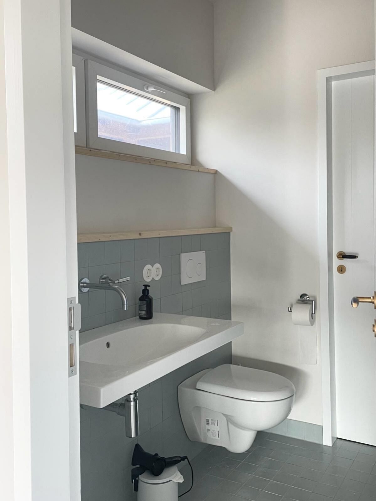 A modern bathroom with a white sink, a toilet, and a window above the sink.