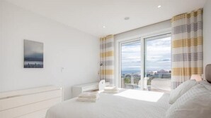 A modern bedroom with a large bed, a bedside table, a window with curtains, and a city view. - Casa Chloe - Luxury Ocean View Apartment (Lagos)