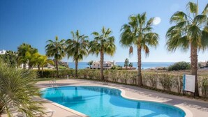 A swimming pool with a curved edge, surrounded by palm trees and a view of the sea. - Casa Chloe - Luxury Ocean View Apartment (Lagos)