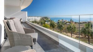 A balcony with wicker chairs and a table, overlooking a coastal landscape with buildings and palm trees. - Casa Chloe - Luxury Ocean View Apartment (Lagos)