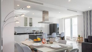A modern kitchen with white cabinets, a black refrigerator, and a dining area with a table set for two. - Casa Chloe - Luxury Ocean View Apartment (Lagos)
