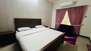 Ein Hotelzimmer mit Bett, Nachttisch, Stuhl und einem Fenster mit Vorhängen.
