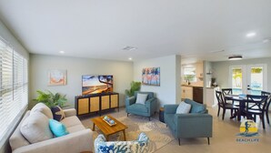 Un salon spacieux comprenant un canapé, des fauteuils, une table basse et un téléviseur. Il y a également un coin repas avec une table et des chaises.