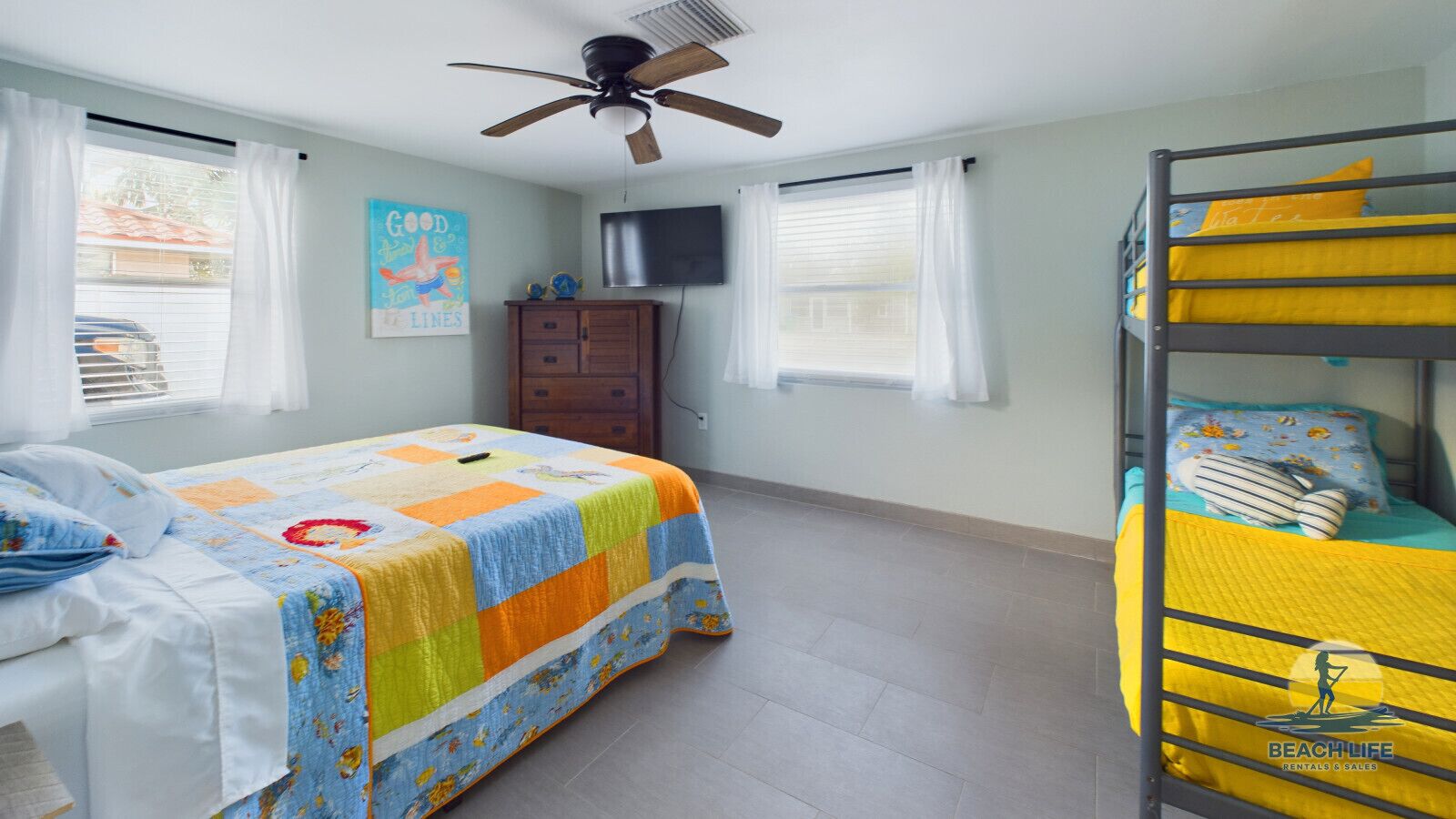 A bedroom with a bunk bed, a single bed, a ceiling fan, a TV, and a dresser.