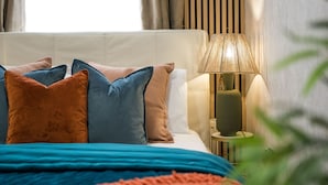 A neatly made bed with a blue and orange blanket, a white headboard, and multiple pillows in shades of blue and brown. - Charming 1-bed Apartment in London (London)