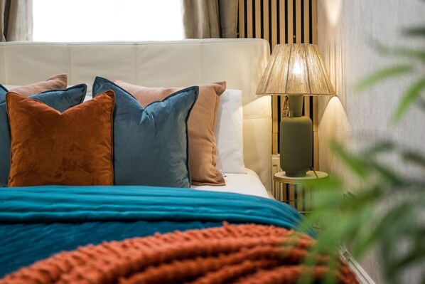 A neatly made bed with a blue and orange blanket, a white headboard, and multiple pillows in shades of blue and brown.