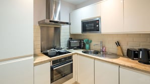 A modern kitchen with stainless steel appliances, white cabinetry, and a wooden countertop. - Charming 1-bed Apartment in London (London)