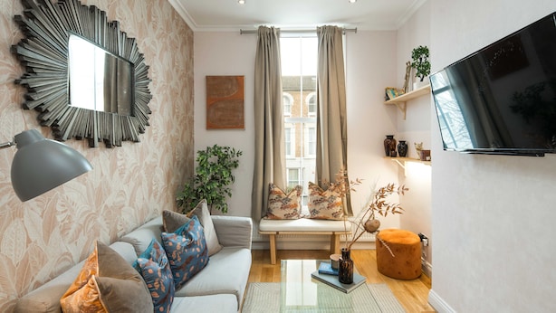 A modern living room with a sofa, a coffee table, a TV, and a large mirror. - Charming 1-bed Apartment in London (London)