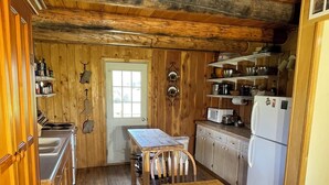 A rustic kitchen with wooden walls and floors, a wooden dining table, and a refrigerator. - The Caddis House- Big Hole River (Melrose)