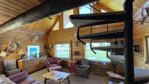 A cozy cabin interior with a wooden ceiling, a spiral staircase, leather furniture, and a view of the outdoors through large windows. - The Caddis House- Big Hole River (Melrose)