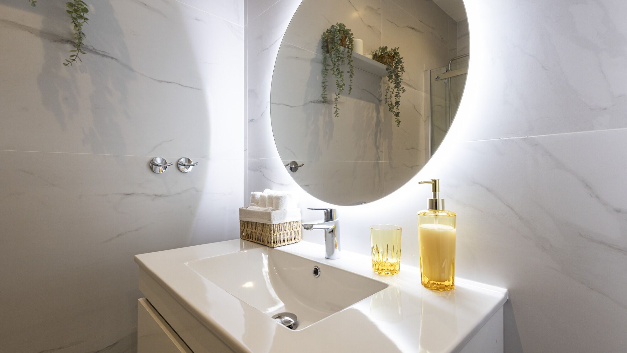 Un baño con lavamanos de mármol blanco, un espejo redondo y cabina de ducha de vidrio.