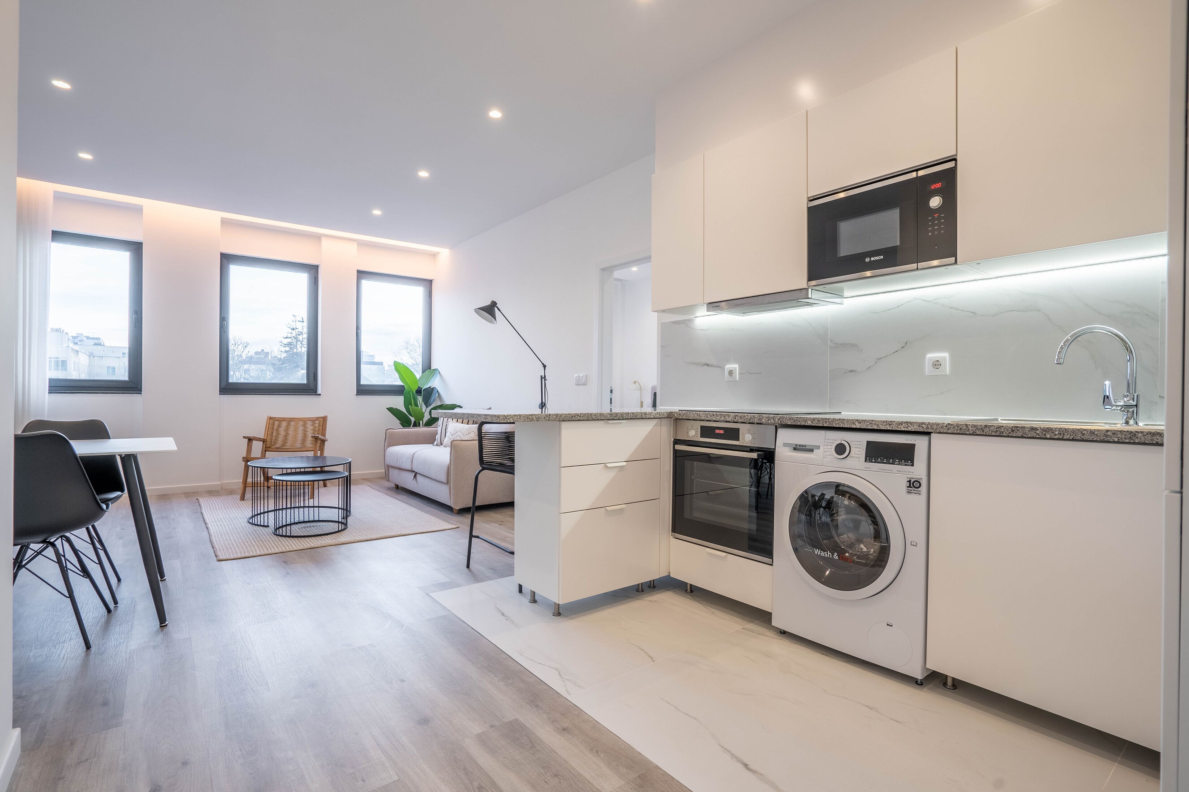 Una cocina moderna con electrodomésticos integrados, un comedor con mesa y sillas, y un amplio ventanal que proporciona luz natural.