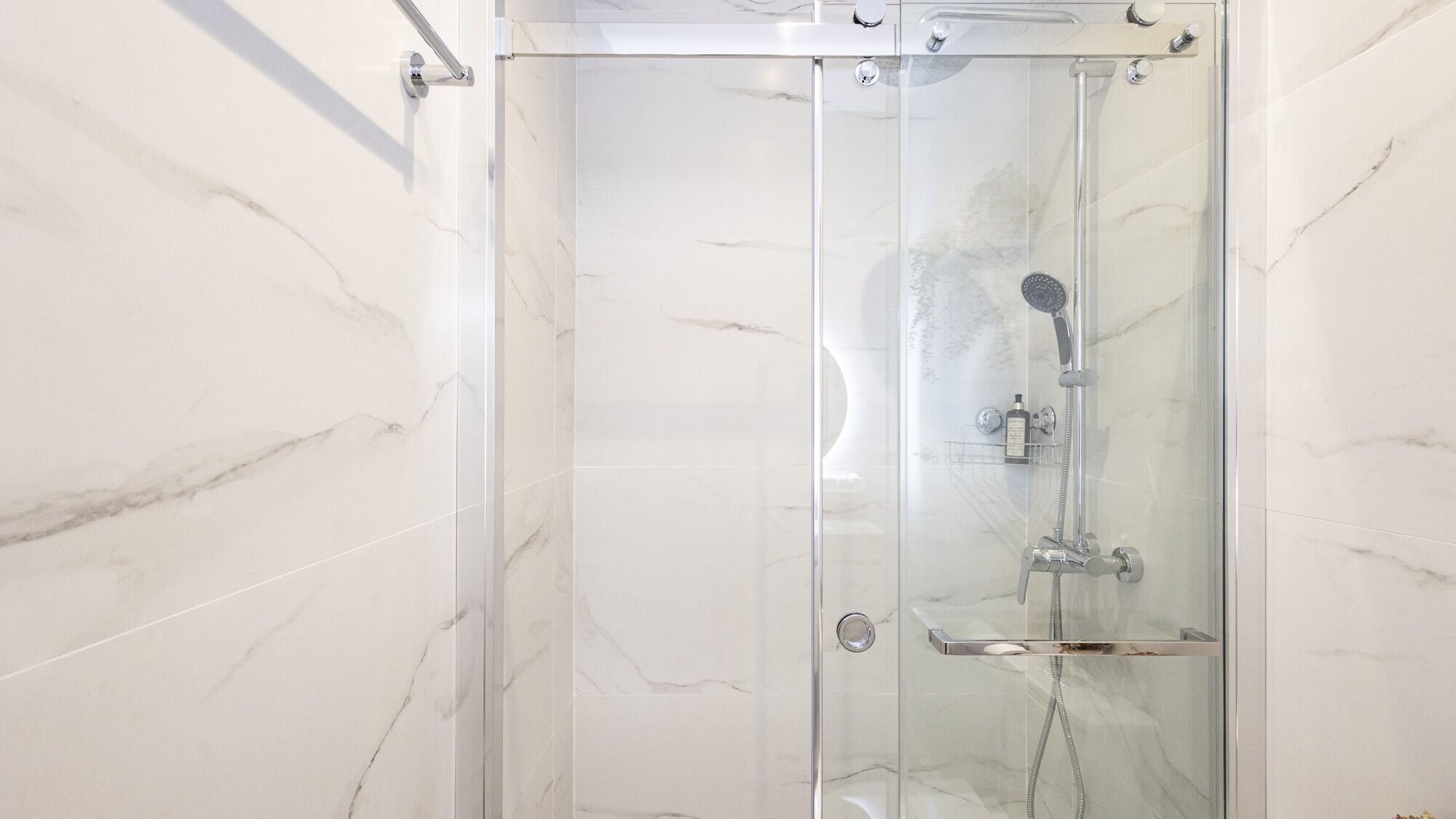 A glass-enclosed shower with a handheld showerhead and a handheld shower attachment.