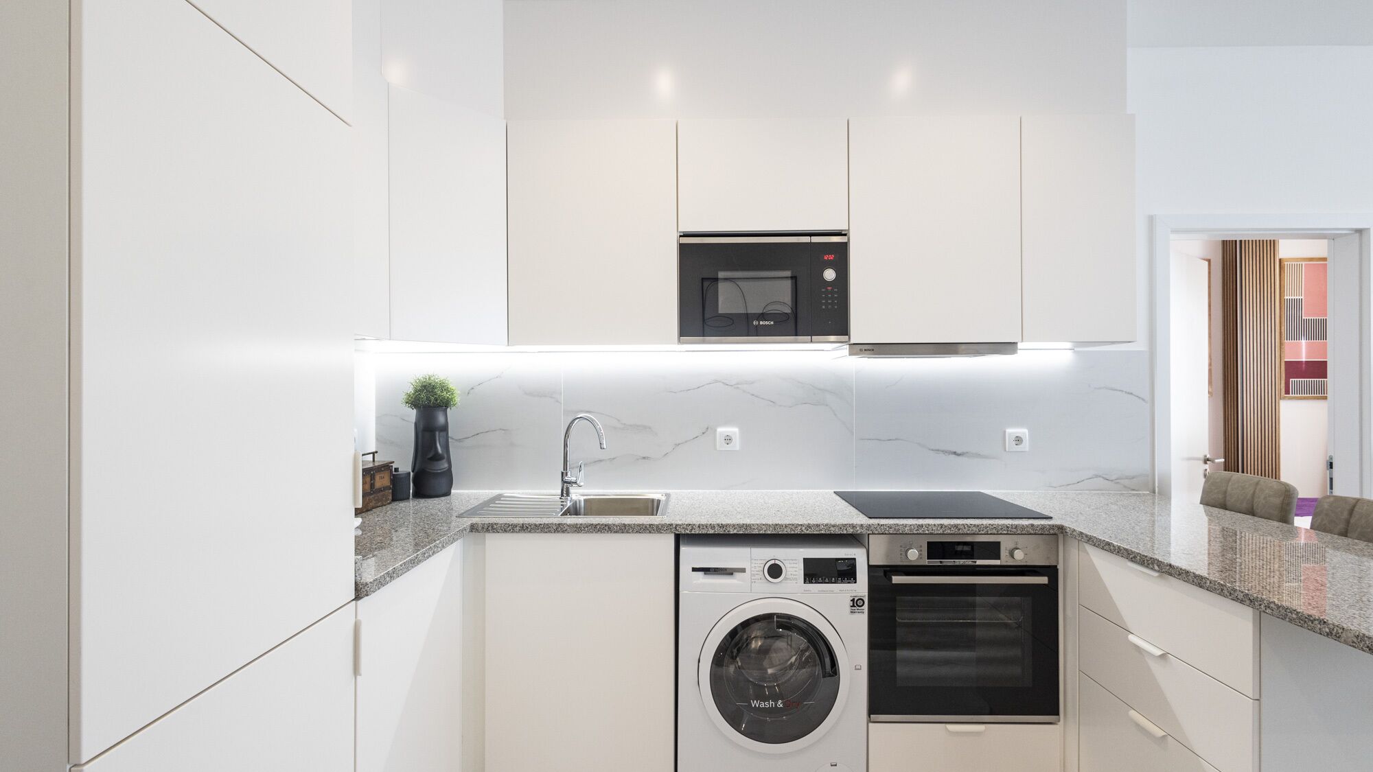 A modern kitchen with white cabinetry, a Bosch microwave, a built-in washing machine, and a dishwasher.