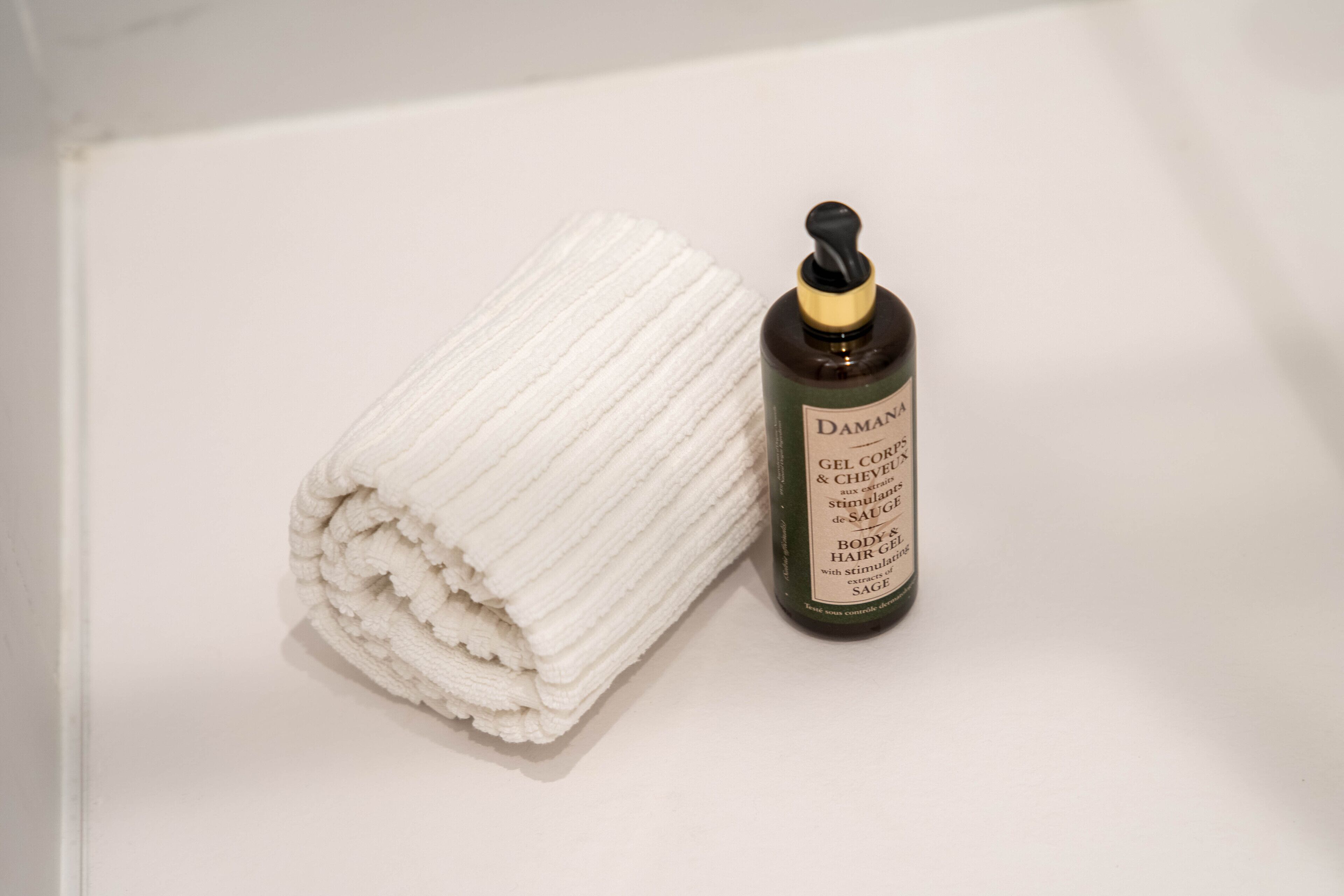 A folded white towel and a bottle of Damani Gel Cream next to it.