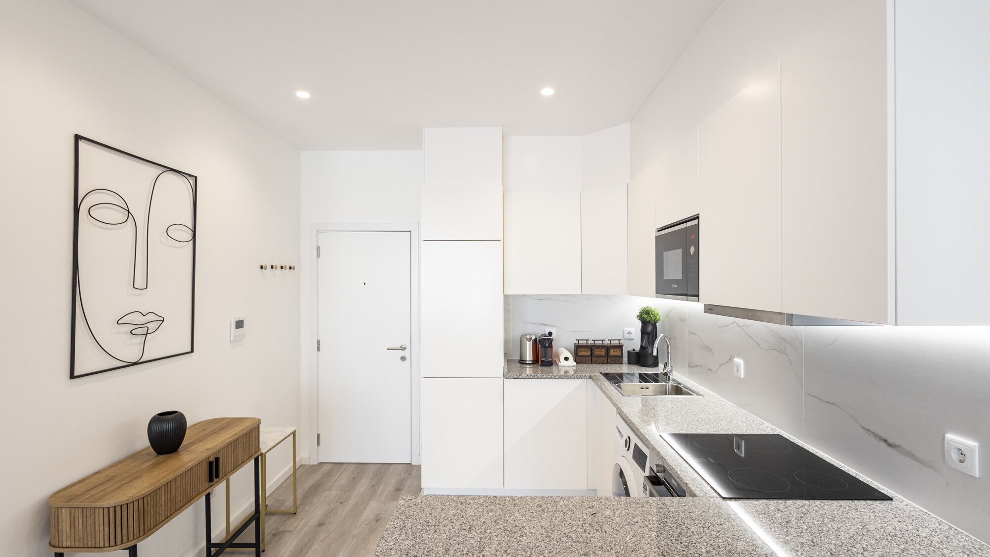 A modern kitchen with white cabinetry, a built-in oven, and a granite countertop.
