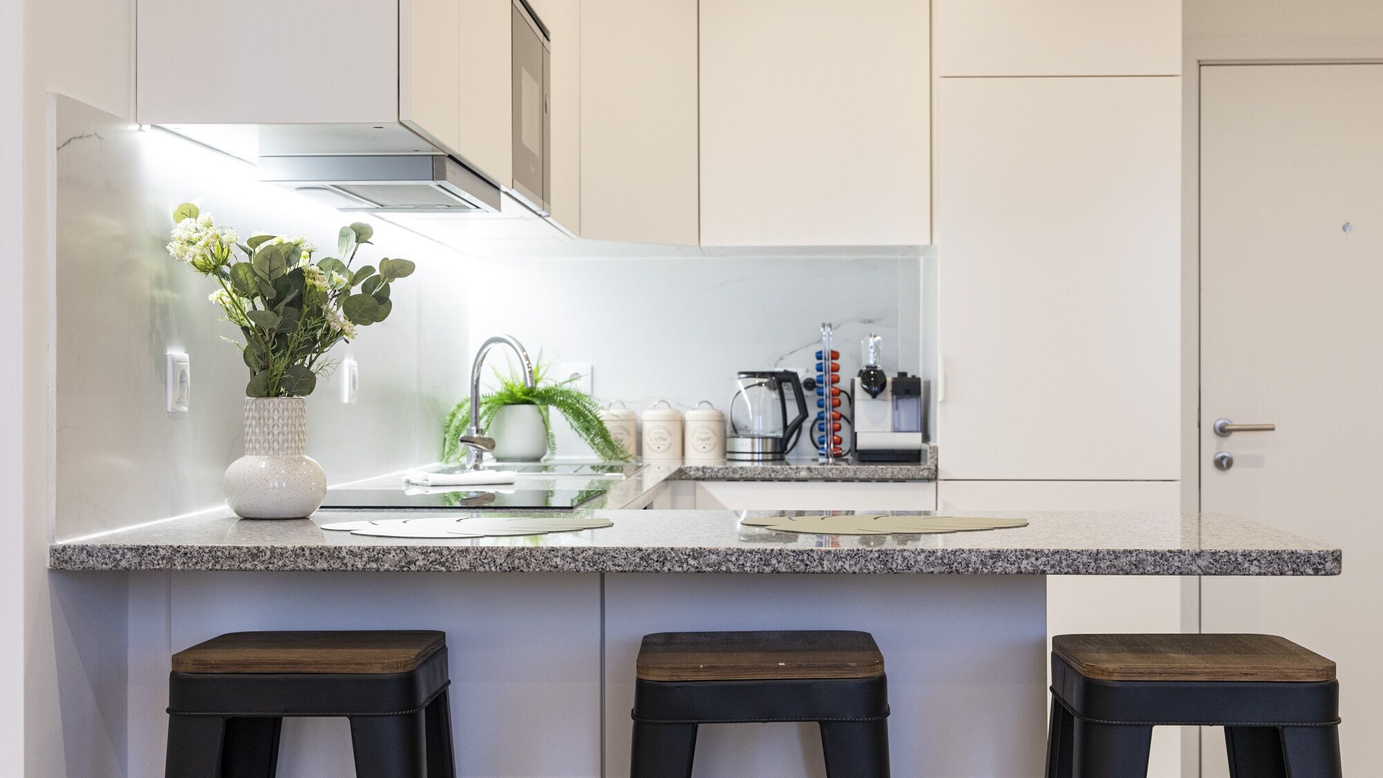 A modern kitchen with a granite countertop, a built-in stove, and three stools.