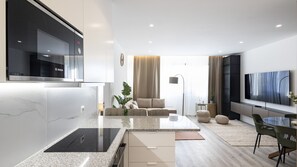 A modern living room with a kitchen area, a sofa set, a dining table with chairs, and a flat-screen TV mounted on the wall. - Skyline Lofts by LovelyStay (Matosinhos)