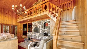 A wooden interior with a stone fireplace, a sofa, and a staircase. - Authentic Swiss Cabin - 4 BR with Hot Tub and pool table (Sainte-Agathe-des-Monts)