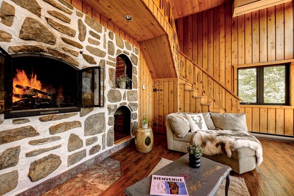 Un interior de cabaña acogedor, con chimenea de piedra, paredes de madera y una zona de estar confortable.