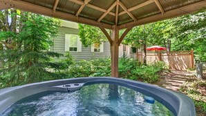 A hot tub under a wooden pergola with a house and lush greenery in the background. - Chalet Boréal, SPA, LAC & SKI (Saint-Donat-de-Montcalm)