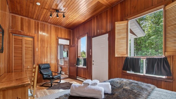 A wooden-paneled room with a bed, a chair, and a window with blinds. - Chalet Boréal, SPA, LAC & SKI (Saint-Donat-de-Montcalm)