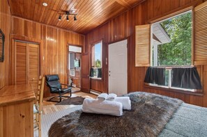 A wooden-paneled room with a bed, a chair, and a window with blinds.